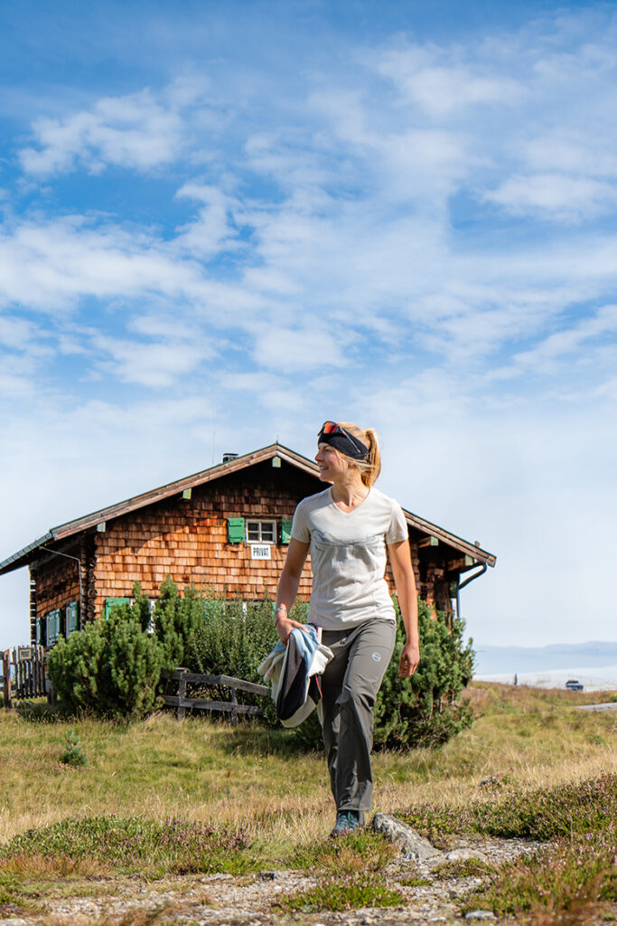 Frau vor einer Hütte in den Bergen mit strahlend blauem Himmel- mit GTS Sports Kleidung
