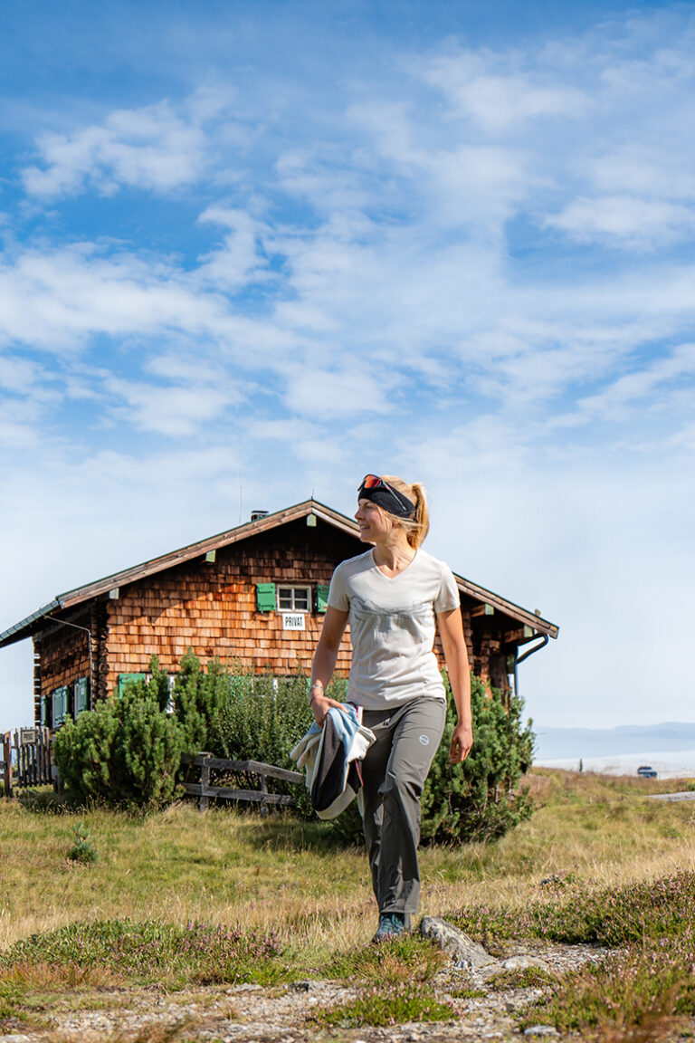Frau vor einer Hütte in den Bergen mit strahlend blauem Himmel- mit GTS Sports Kleidung