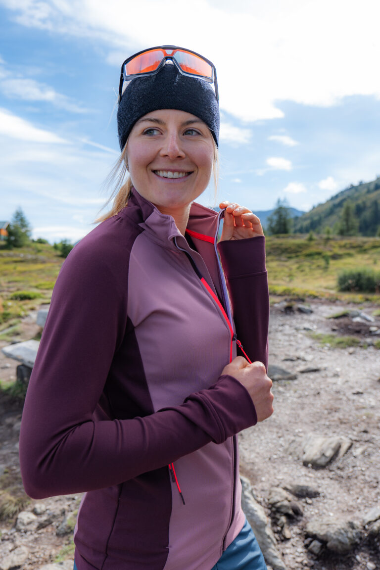 Frau mit lilafarbener GTS Sports Kleidung und Sonnenbrille auf einem Berghang